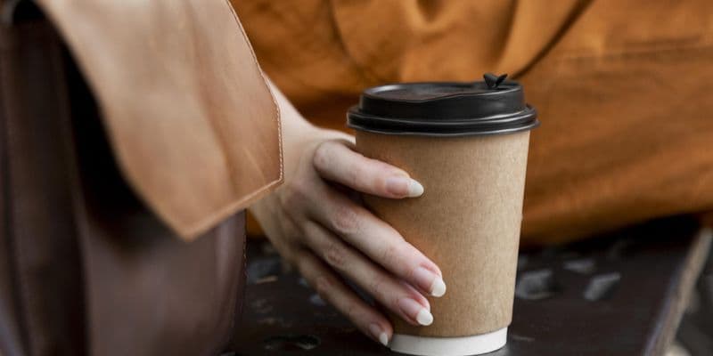 Mujer en un banco con un envase de café - Foto de Freepik